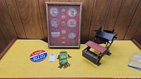 Full view of framed pins with accompanying items on table: green ribbon, large Labor for Rizzo pin, and black miniature chair