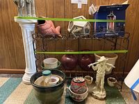 Black metal plant stand with various planters and decorative items arranged on and around it.