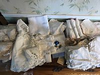 Overview of folded embroidered handkerchiefs, lace doilies, and linens, including one with floral embroidery.