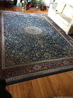Full view of the large Oriental style area rug laying on hardwood floor with visible blue central floral pattern and cream medallion.