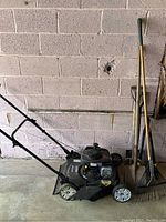 Side view of Murray lawn mower along with garden tools (metal rake and shovels)