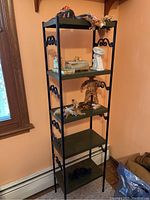 Full view of tall black metal shelf with five green wooden shelves and various decorative items arranged on top shelves.