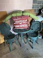 Green metal outdoor bistro table and 2 chairs with stacked cushions