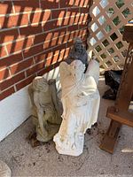 Photo showing three outdoor statues together: gray angel, white St Michael, and gray St Francis against a brick wall.