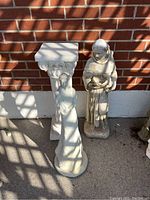 Overview of Moses statue, garden lady statue, and pedestal leaning against brick wall, showing size and condition.