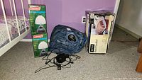 Photo of two boxed Coleman table lamps next to a box for the Aero Raised Airbed and a deflated blue Aero air mattress with electric pump on carpeted floor.