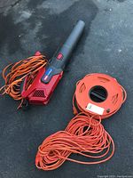 Overall photo showing the Toro PowerJet F700 leaf blower lying on the ground with two orange extension cords, one coiled on an orange cord reel.