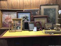 Wide shot showing multiple framed wall art pieces and empty frames arranged on a table with wood paneled background