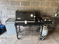 Front view of Weber Silver gas grill with side burner, grill lid closed, propane tank attached.