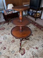 Full view of the three-tier round wooden table showing the shape, size, and condition in a room setting.