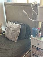 Side-view photo showing the gray upholstered headboard with nailhead trim and matching bed frame with pillows and bedding.