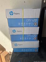 Three stacked boxes of HP Office20 printing paper reams, sealed with a yellow plastic strap, showing brand and product series on box.