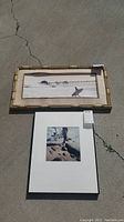 Two framed beach photographs displayed on the ground, one with bamboo-style frame and one with black slim frame.