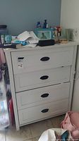 Front view of the white four-drawer dresser covered with miscellaneous personal items.