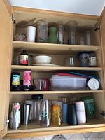 Overview of wooden cabinet shelves containing various vases, mugs, drink flasks, and plastic containers.