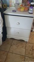 Full front view of the white wooden nightstand showing two drawers with round knobs and curved bottom edge.