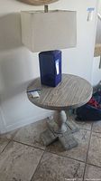 Full view of the occasional table with faux wood veneer top and pedestal base, shown with a large rectangular beige lamp on top.