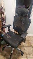 Front angle view of black mesh office chair with headrest and armrests on casters.