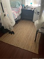 Full view of the woven organic rug placed in a room beside furniture showing size and color.