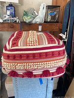 Pouf ottoman showing top and side patterns with decorative pink and cream stripes and textured bobbles.