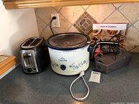 Overall view of Black & Decker toaster, Rival crockpot, and three hand mixers including one boxed Purple Carrot model