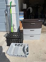 Shows three-drawer plastic storage unit, gray plastic dish rack, black crate, and green mop leaning against metal clothes hanger stand
