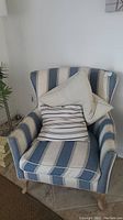 Upholstered armchair with blue and white vertical stripes, three pillows arranged on seat (two beige and one blue/white striped)