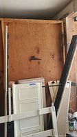 Bed frame pieces including side rails, footboard, and support slats leaning against plywood wall.