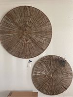 Wide shot of two woven rope wall art pieces, one larger and one smaller, hanging on a white wall