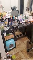 View of the wood desk with various items on and underneath, cluttered but showing the desk structure and finish.