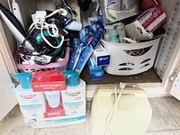Photo showing vintage hair rollers, curling irons, Eucerin lotions, toothbrushes, toothpaste, cleaning wipes, and plastic baskets under a sink.