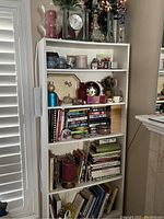 Full view of white bookshelf filled with books, candles, vases, clock, and collectibles.