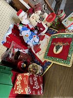 Photo showing Christmas plush figures including Santa and snowman, assorted candles, tins, and decorative holiday linens.