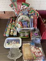 Photo of assorted Christmas party supplies including plates, napkins, wrapping paper, gift tags, cups, and ornaments packed in a box