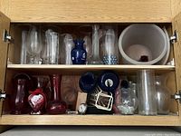 Shelf cabinet with various clear, blue, and red glass vases and containers, some holding beads or decorative items.