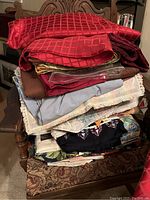 Stack of various folded tablecloths and linens showing colors in red, brown, gray, and patterned fabrics