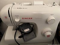 Front right side view of white Singer Tradition sewing machine with foot pedal placed in front of machine.