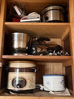 Full view of wooden shelf with kitchen appliances including crock pots, metal mixing bowl, attachments, and a small roaster.