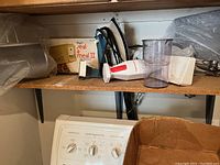 Overall shelf view showing Seal-a-Meal box, immersion blender, iron barbecue tools, and iron pan.