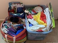 Overview of a large bin filled mostly with colorful tissue paper and some flat gift bags with Santa Claus and holiday themes