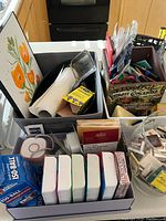 Photo showing large boxes filled with vintage matchbooks, a framed poppy flower picture, a rustic lantern, pill organizers, paper towels and other small items in kitchen setting.