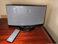 Bose Sound Dock speaker with front grille and remote control placed on a wooden surface.