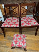Pair of wooden armless chairs with upholstered red geometric pattern seats and footstool in front.
