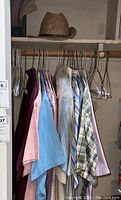 Overview of hanging men's XXL button-up shirts in various colors and patterns with straw hat on shelf above.