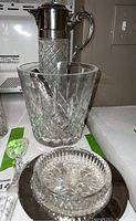 Photo of crystal ice bucket with metal tongs and glass carafe with silver-tone spout and handle.