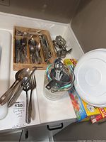 Kitchen counter view showing Pyrex measuring cups, measuring spoons, white cutting board, silver serving piece and cutlery in a tray