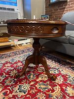 Side view of round wood end table showing circular carved details around edge and drawer opening
