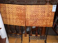 Two folding tray tables with woven geometric patterned tops and black metal bases with crisscross design, folded and standing upright.