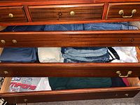 Three drawers filled with men's clothing: denim jeans, shorts, and t-shirts visible in assorted colors and folded.