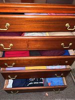 Five wooden drawers containing folded men’s clothing including sweaters and shirts in XXL size.